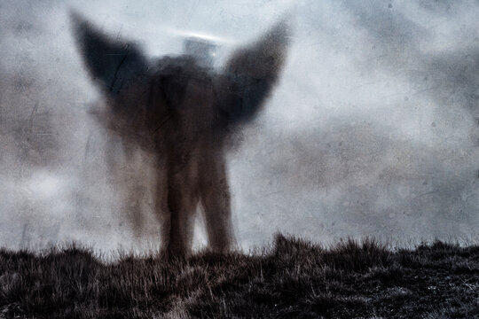 A horror, spiritual concept of a scary angel figure with glowing eyes standing outside. With a grunge textured edit.