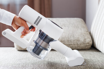 A person uses a white cordless vacuum cleaner to clean the sofa in the living room.