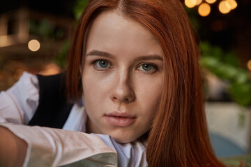 young caucasian stylish redhead pretty woman with long hair lays her head on her arms and table....