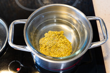 above view of dried crushed medicinal herbs and plants in glass bowl in stewpot on ceramic hob at home kitchen