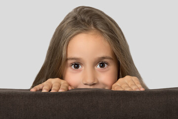 A child, a little girl, hides and looks out from behind the sofa. Childish curiosity.