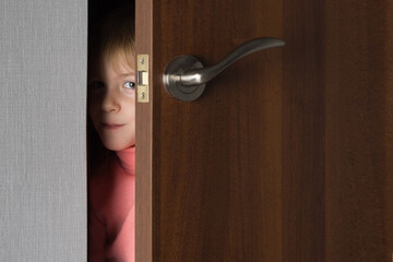 A child, a little girl, looks out from the ajar door of the room. Childish curiosity.