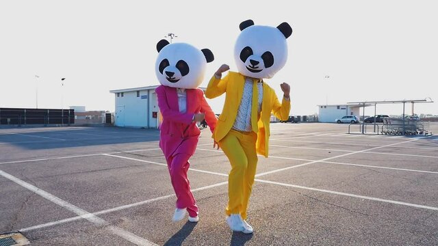 Happy people wearing a panda giant head dancing and having fun in a parking lot