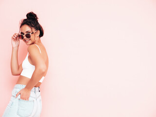 Young beautiful smiling female in trendy summer clothes. Sexy carefree woman posing near pink wall in studio. Positive brunette model having fun and going crazy. Cheerful and happy in sunglasses