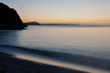 Fototapeta na wymiar Beautiful sunrise over Pentewan Sands in Cornwall with pastel sky and long exposure ocean