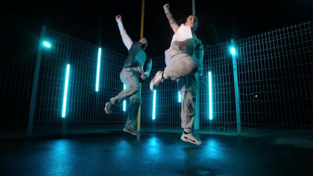 Young dancers practicing dance routine at night with neon lights. Afrodance. Professional dancers dancing hip hop outdoors. Man and woman. Youth culture. Slow motion in 4K, UHD