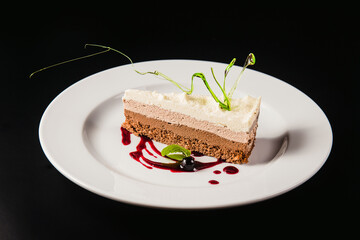 Layered coffee cake with decoration on a round white plate on a black background