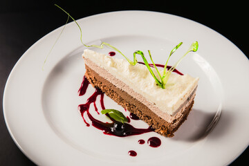 Layered coffee cake with decoration on a round white plate on a black background