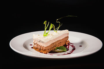 Layered coffee cake with decoration on a round white plate on a black background