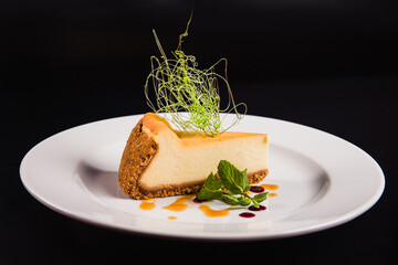 Cheese cake with decoration on a round white plate on a black background