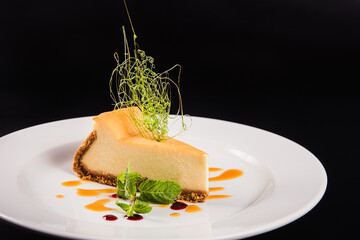 Cheese cake with decoration on a round white plate on a black background
