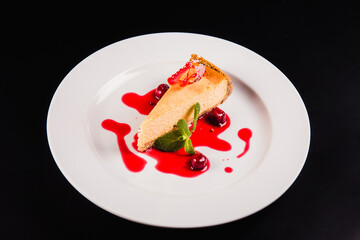 Berry cake with decoration on a round white plate on a black background