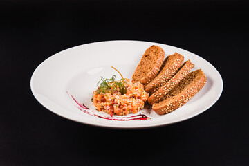 Salad with salmon and brown bread on a white plate on a black background. Tartar