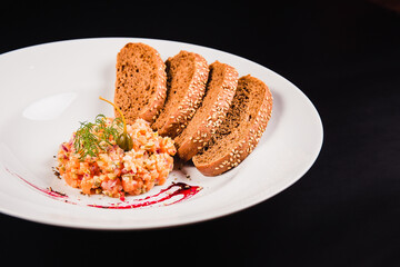Salad with salmon and brown bread on a white plate on a black background. Tartar