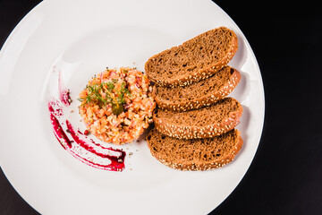 Salad with salmon and brown bread on a white plate on a black background. Tartar