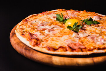 Round pizza with an egg on a wooden board on a black background