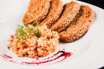 Salad with salmon and brown bread on a white plate on a black background. Tartar