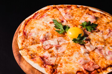 Round pizza with an egg on a wooden board on a black background