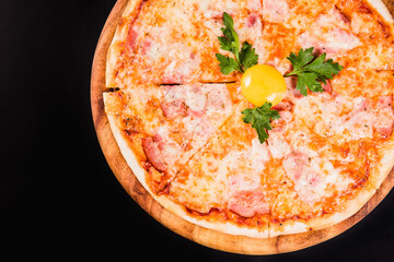 Round pizza with an egg on a wooden board on a black background