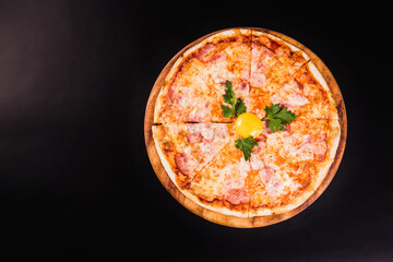Round pizza with an egg on a wooden board on a black background