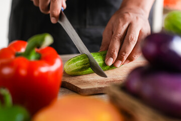 Front view Chef hold knife in hand and cut cucumber on cutting board in modern society popular concept