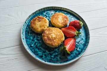 Сheese pancake, сheesecakes with fresh strawberries on a blue plate on a white wooden table background