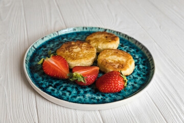 Сheese pancake, сheesecakes with fresh strawberries on a blue plate on a white wooden table background