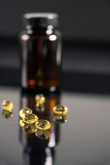 The tablets lie on a mirrored black background, reflect in it. Dark bottle with medicine out of focus.