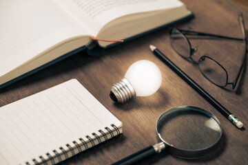 Closeup glowing light bulb in the group of story creator instruments, reading and writing idea