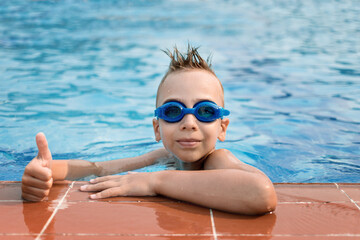 Boy in blue goggles for swimming in the pool. Summer vacation of a child in the pool.