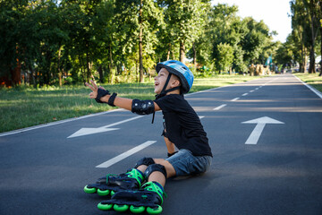 The boy is rollerblading on the track in the city park. The child learns to roller-skate. An active walk with a child on the street.The boy fell on the asphalt on roller skates.