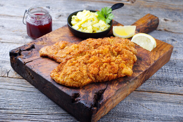 Traditional deep-fried schnitzel with potato salad and cranberries served as top view on an old rustic wooden board at a mountain chalet