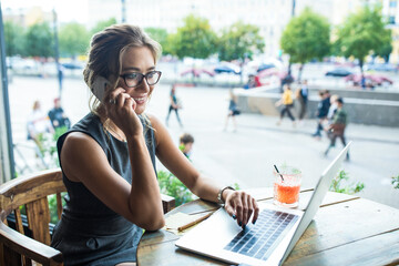 Happy smiling woman skilled marketing coordinator talking via mobile phone during work on laptop...