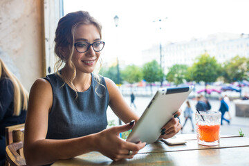 Cheerful woman publication specialist reading articles on web site via digital gadget while sitting in coffee shop during work break. Smiling female having online video conference via touch pad © ZoFot