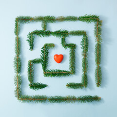 Natural maze made of fir branches and red heart on bright blue background. Minimal love concept....