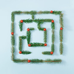 Natural maze made of fir branches and red decoration on bright blue background. Minimal Christmas or New Year concept. Creative nature flat lay composition.