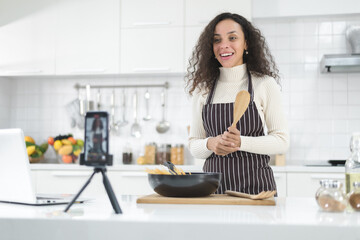 Latin women live streaming online with a smartphone while cooking in the kitchen at home.