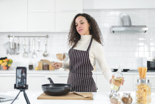 Latin Women Live Streaming Online With A Smartphone While Cooking In The Kitchen At Home.