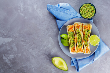 Tacos with fried minced meat and guacamole on a gray plate. Mexican tacos and lime slices on a gray...