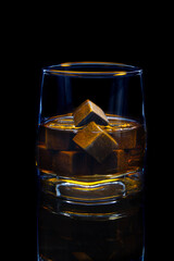 Whiskey in glass with grey whiskey cooling stones on black background