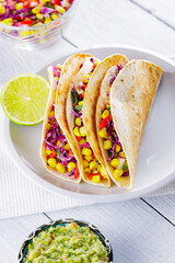 Mexican tacos with different vegetables and guacamole on white boards. Vegan tacos with corn, purple cabbage and tomatoes on a white plate. Mexican cuisine