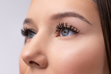 Fototapeta premium Close up portrait of woman face. Young, beautiful girl with fresh soft skin combing long black eyelashes with special mascara brush. Fake eyelashes. Eyelashes extensions close up