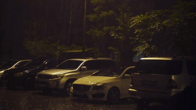 BATUMI, GEORGIA - September 21, 2021: There are parked cars in a row in the courtyard of the house. It's raining heavily and lightning flashes illuminating everything. Night time.