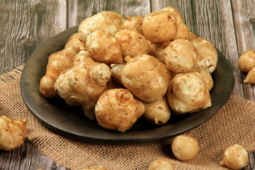 Raw Jerusalem artichoke in a clay bowl on wooden boards background. Raw Organic topinambour