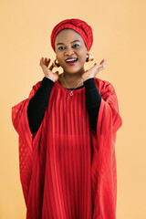 Beautiful emotional smiling woman with bright makeup against yellow background. Studio shot of female African model in ethnic red dress and shawl looking at camera and smiling.