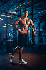 Naklejka na ściany i meble Portrait of young man, muscled athlete, bodybuilder posing at sport gym, indoors. Concept of sport, activity, healthy lifestyle