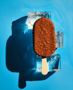 Chocolate nut ice cream on ice cubes on a blue background. Sunlight. Summer concept