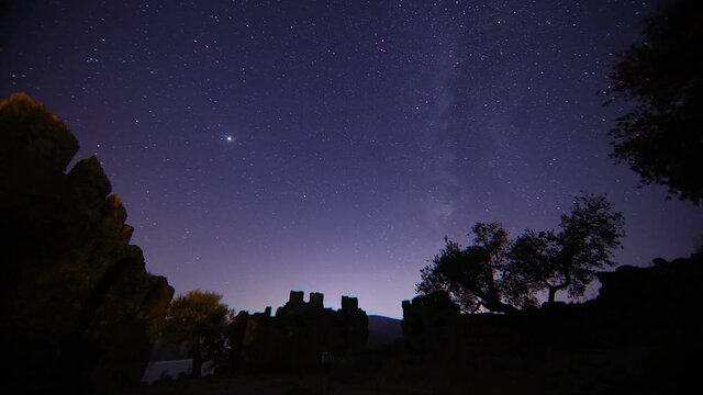 old castle in the night. Timelapse of moving star trails in night sky. A view of the stars of the Milky Way with a mountain top in the foreground. Perseid Meteor Shower observation.