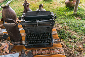 old typewriter surrounded by ceramics on a traditional table with traditional blanket queros plates, glasses and cultural basijas from the Andes of Peru