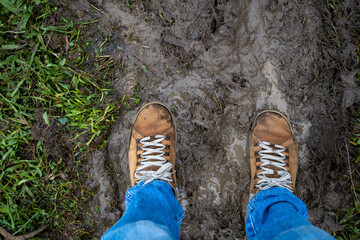 Top view photo of engineering man wearing jeans and brown leather shoes standing on muddy ground after heavy rain